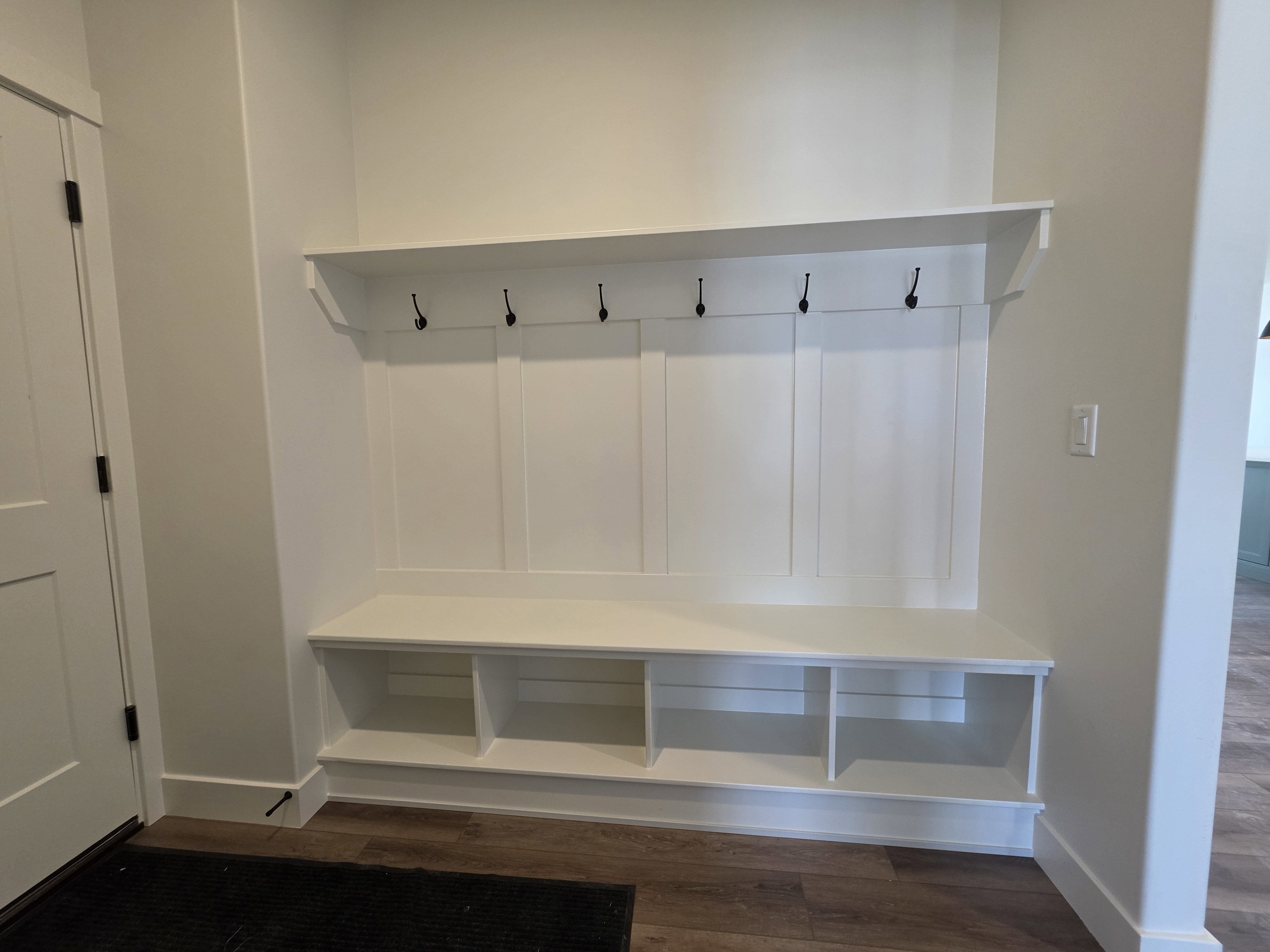 Built-in mudroom bench with three storage cubbies, five coat hooks, and an overhead shelf, set against a wainscoting-style wall paneling