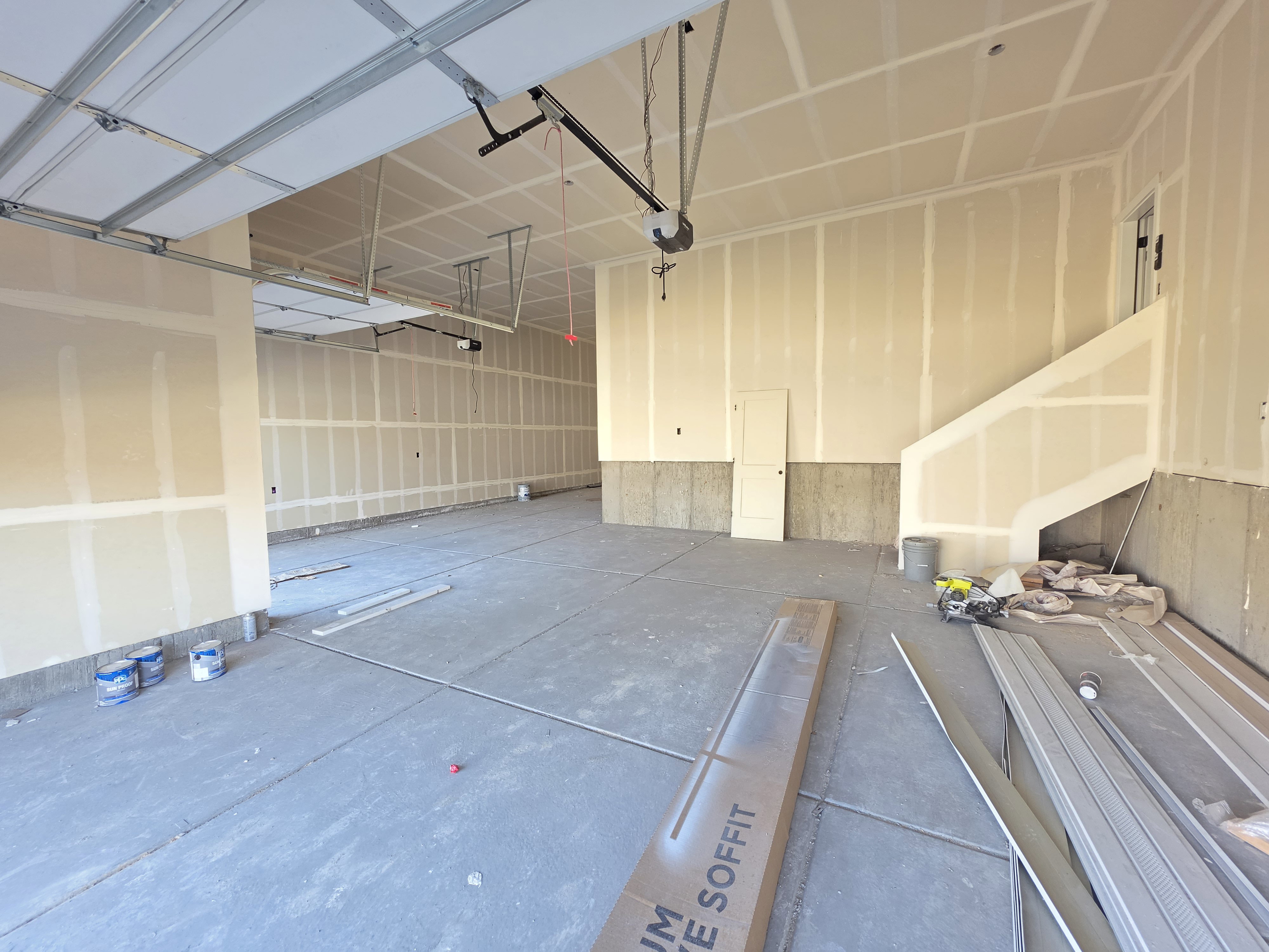 Spacious garage featuring a concrete floor, exposed ceiling joists, and a partial staircase