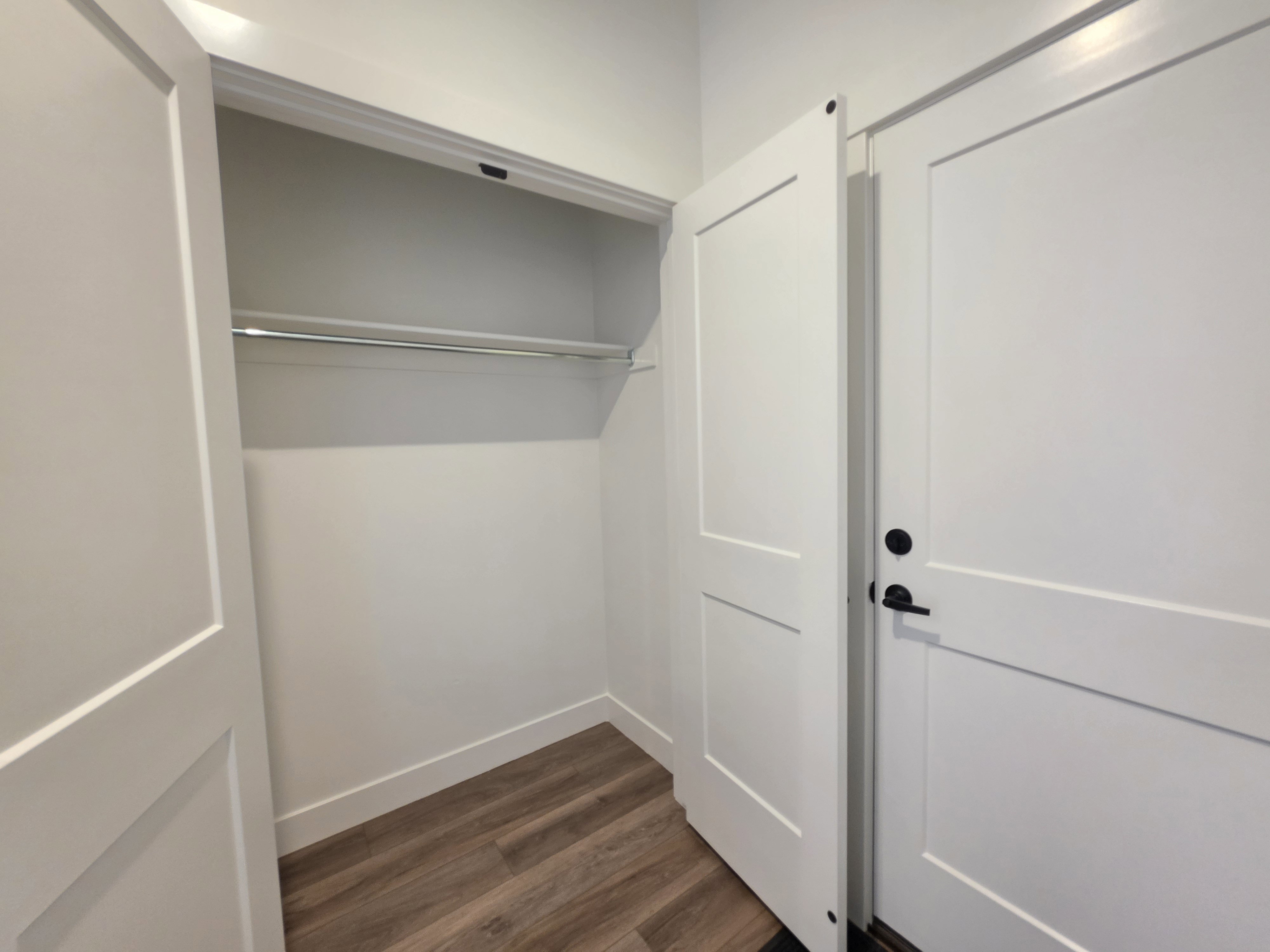White two-panel interior doors with matte black hardware, wood-finish flooring, and white baseboards