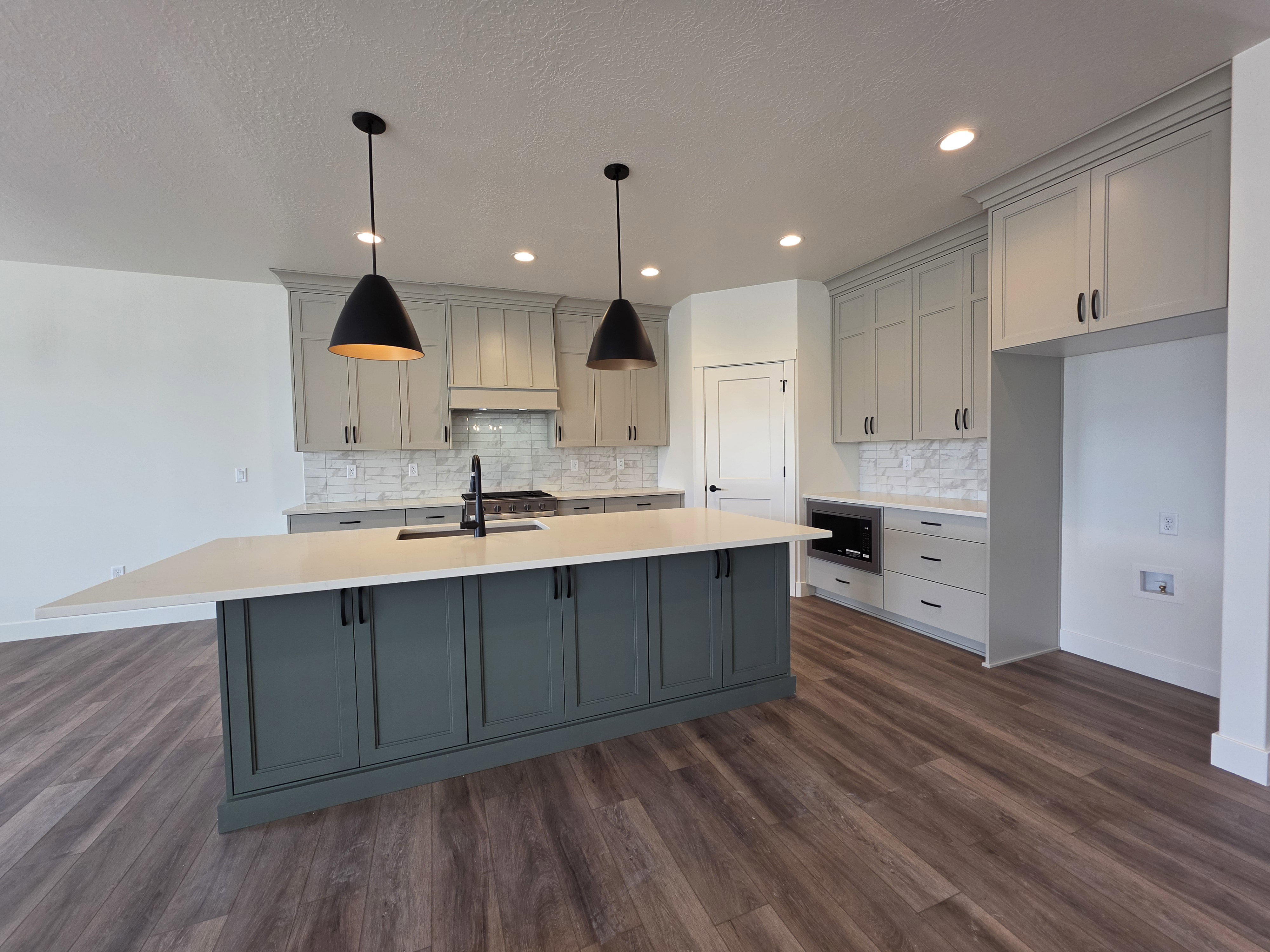 Spacious kitchen featuring a large island with a countertop extension, light-colored perimeter cabinetry, and wood-finish flooring