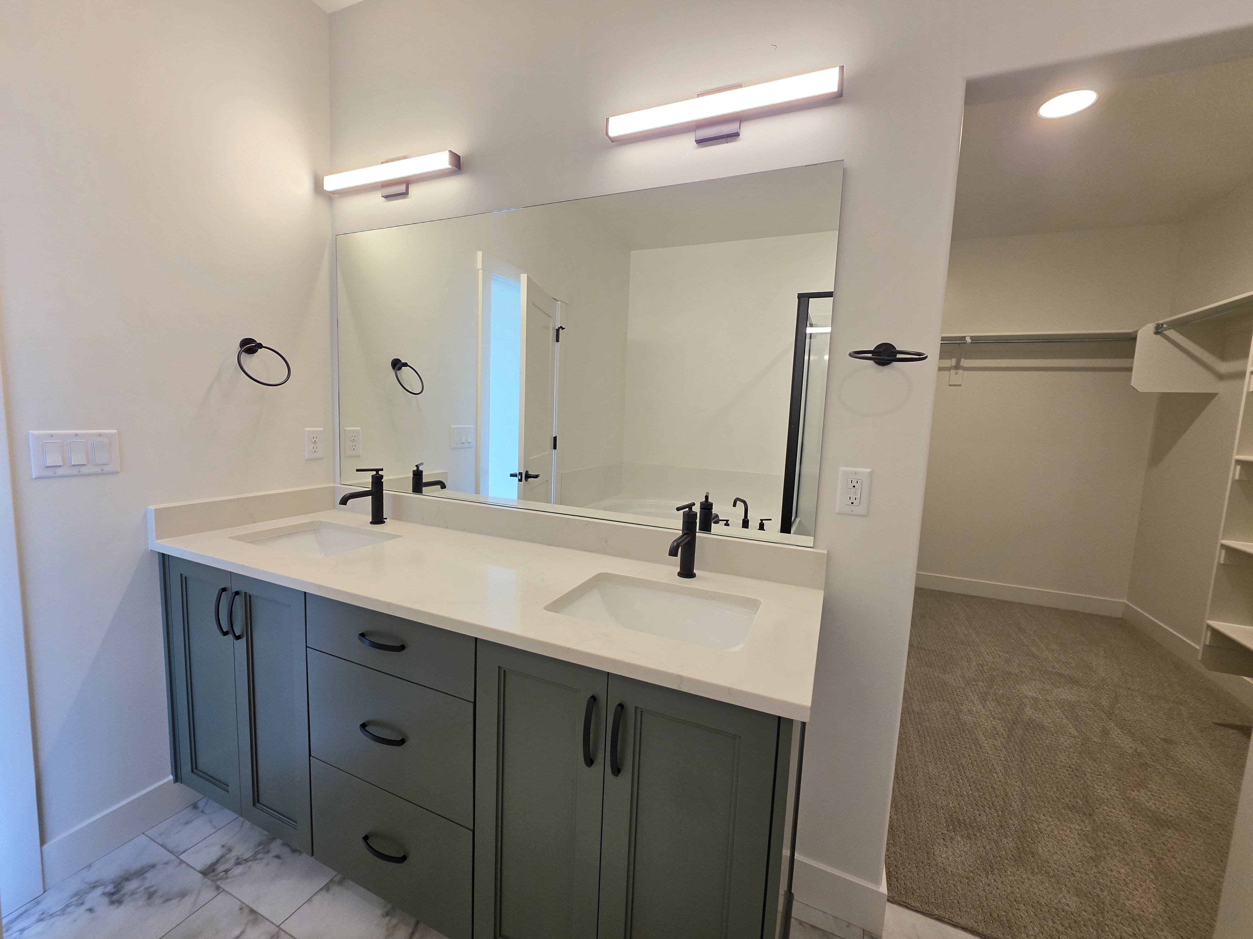 Dual vanity with light-colored countertops, matte black fixtures, and green cabinetry