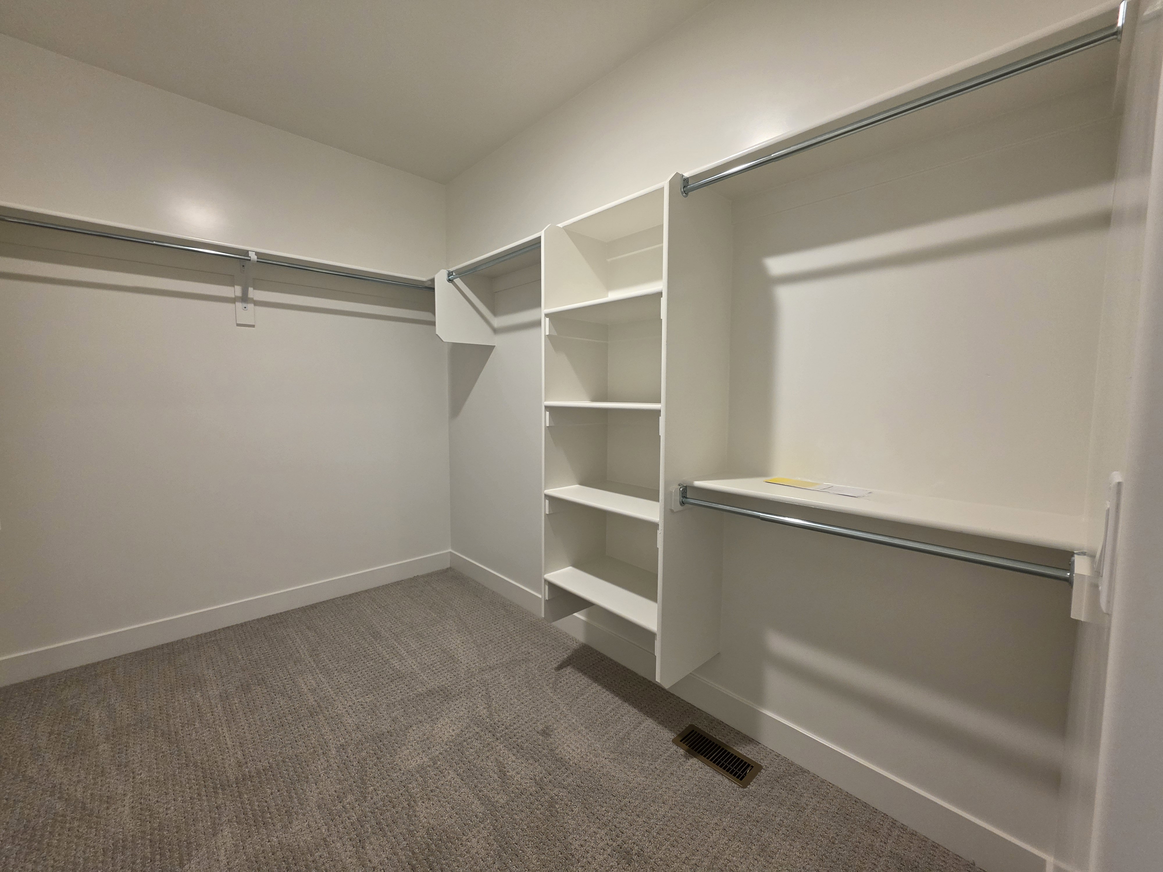 Walk-in closet with integrated shelving units, multiple chrome hanging rods, and neutral carpet flooring