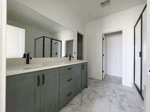 Full bath featuring a shower stall, light marble finish flooring, and double vanity