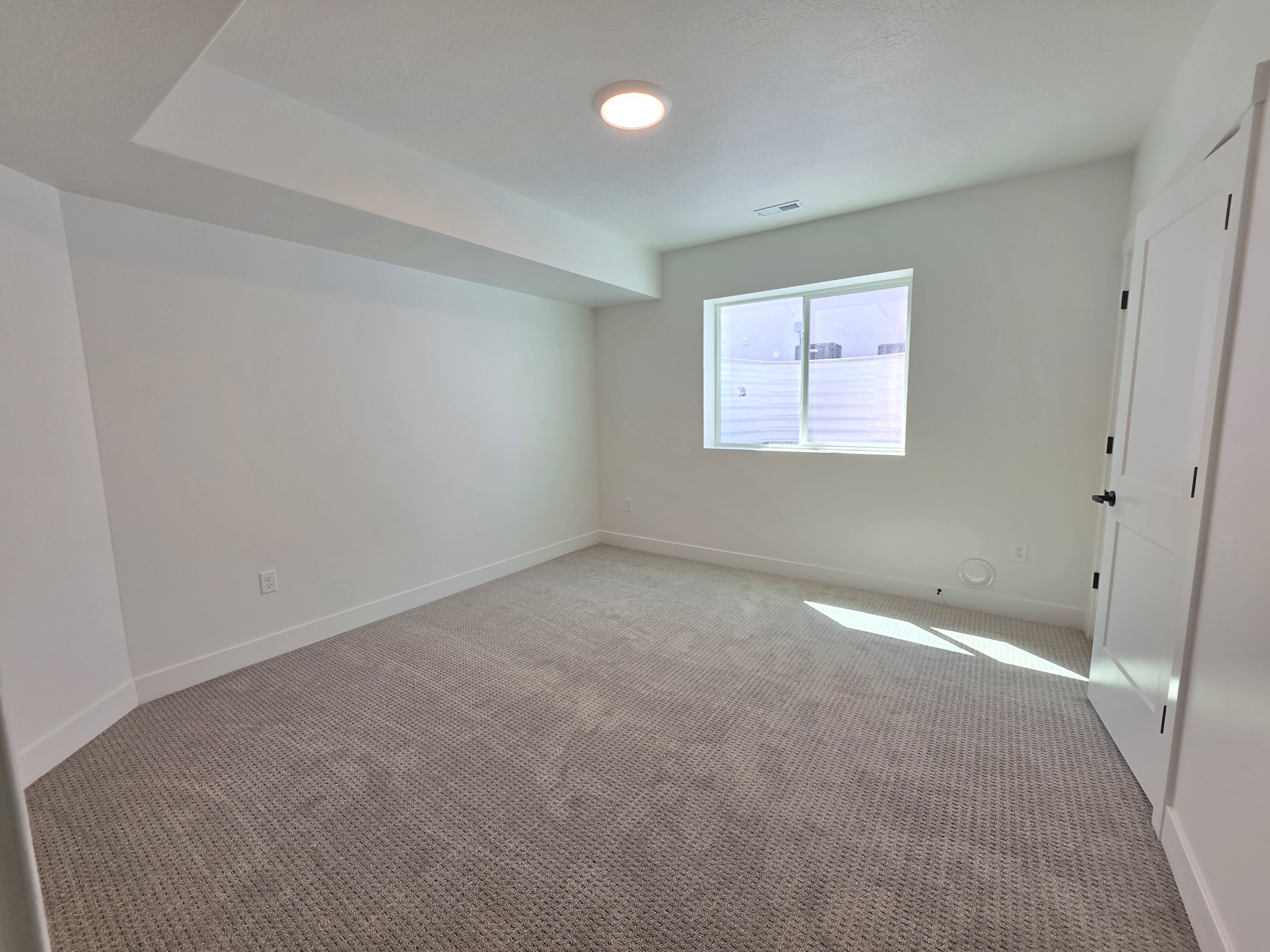 Carpeted room featuring a single window with blinds, a white paneled door with black hardware, and a recessed ceiling light
