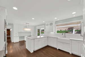 Kitchen with a peninsula, white cabinets, elegant backsplash, and decorative light fixtures