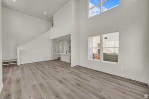 Unfurnished living room featuring plenty of natural light, a high ceiling, light wood-style flooring, and recessed lighting