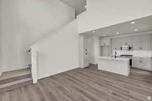 Kitchen with stainless steel appliances, a high ceiling, a center island with sink, decorative backsplash, and light wood-type flooring