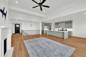 Living room with light wood finished floors, ceiling fan, a fireplace with raised hearth, and recessed lighting