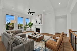 Living room featuring wood finished floors, a ceiling fan, a warm lit fireplace, beamed ceiling, and recessed lighting