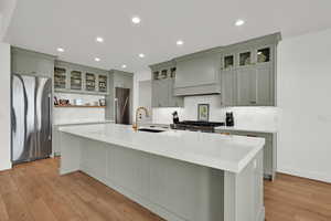 Kitchen with stainless steel fridge, glass fronted cabinets, decorative backsplash, light wood-type flooring, and recessed lighting