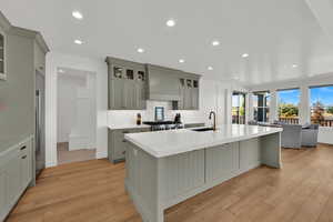 Kitchen with glass insert cabinets, recessed lighting, decorative backsplash, a kitchen island with sink, and light stone counters