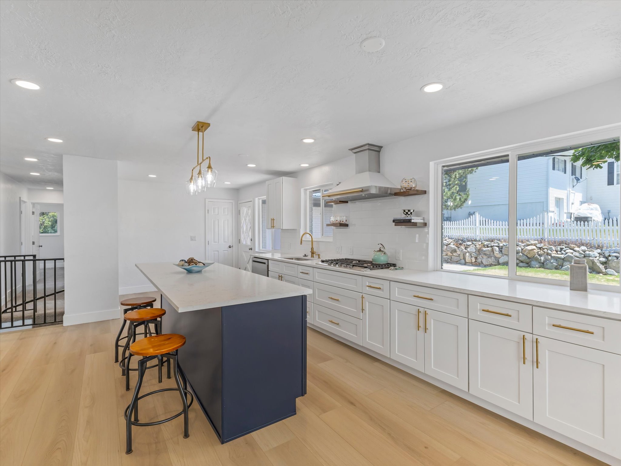 Contemporary kitchen featuring a large central island with a contrasting navy base, light wood-finish flooring, white shaker-style cabinetry with brass hardware, a white tile backsplash, and extensive countertop space