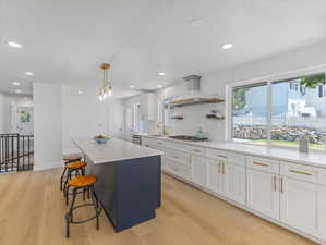 Contemporary kitchen featuring a large central island with a contrasting navy base, light wood-finish flooring, white shaker-style cabinetry with brass hardware, a white tile backsplash, and extensive countertop space