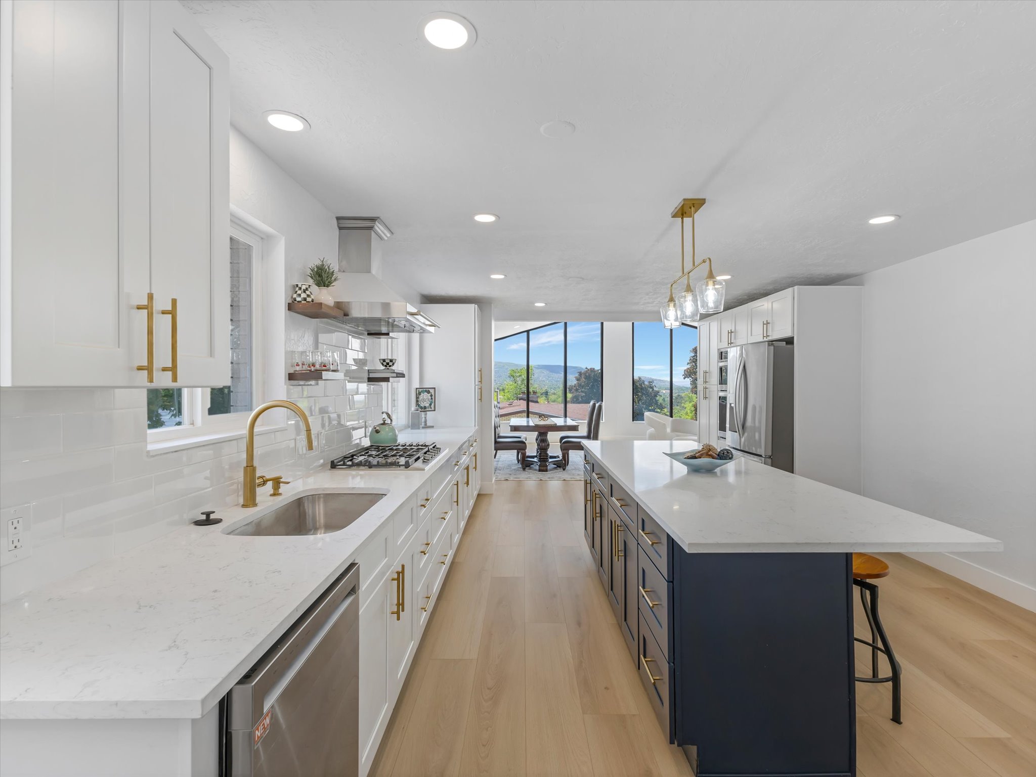 Contemporary kitchen featuring white shaker cabinetry, gold-tone hardware, light-toned wood-finish flooring, and a contrasting island with a light countertop