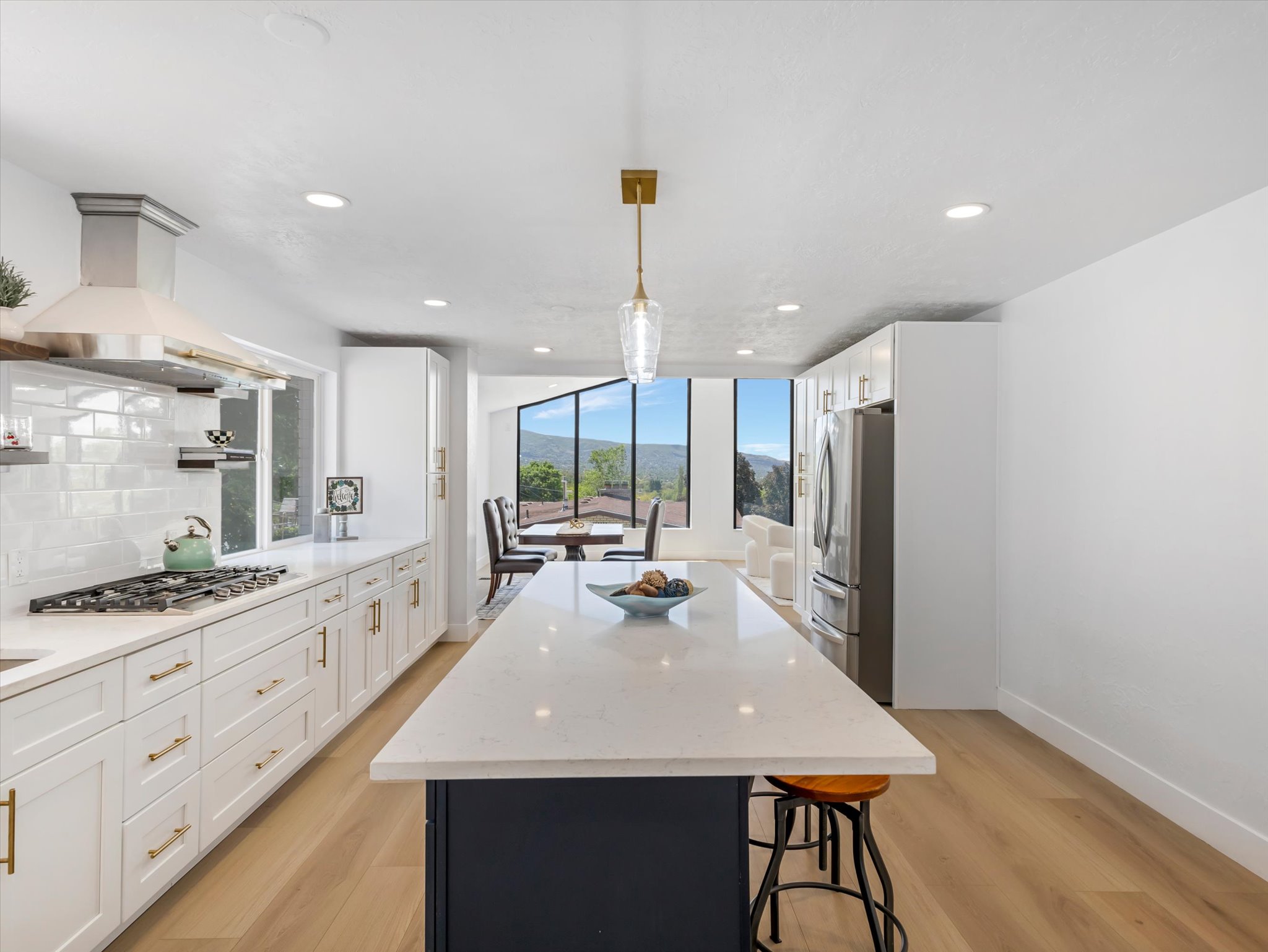 Contemporary kitchen featuring a large central island with seating, white shaker cabinetry, stainless steel appliances, and wood-finish flooring
