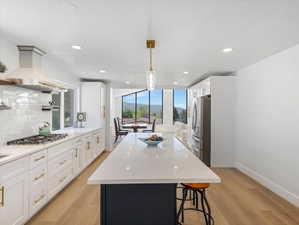 Contemporary kitchen featuring a large central island with seating, white shaker cabinetry, stainless steel appliances, and wood-finish flooring