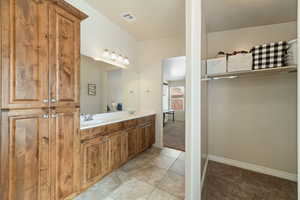 Full bath featuring double vanity, light tile patterned floors, light carpet, and a spacious closet