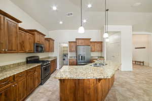 Kitchen featuring stainless steel appliances, light stone countertops, wood finish cabinetry, and hanging light fixtures