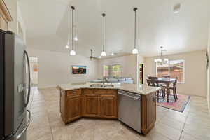 Kitchen with stainless steel appliances, lofted ceiling, a kitchen island with sink, a ceiling fan, and light stone counters