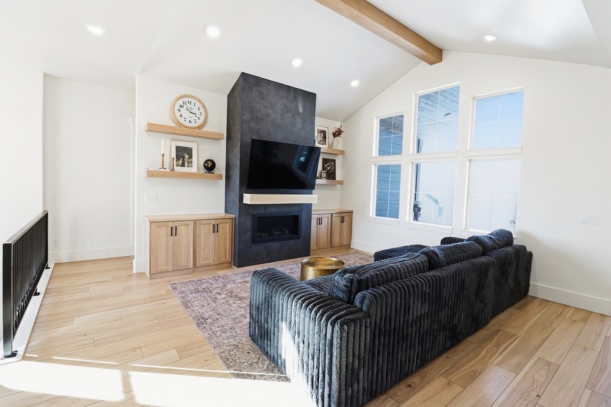 Vaulted ceiling with exposed wood beam, contemporary fireplace with dark surround, light wood-finish flooring, custom built-in cabinetry, and multi-pane windows