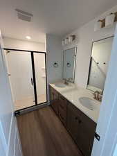 Full bath featuring a stall shower, double vanity, a textured ceiling, and dark wood-type flooring