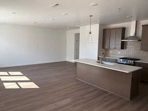 Kitchen featuring gas stove, an island with sink, light stone counters, and dark wood finished floors