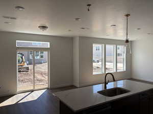 Kitchen with light stone countertops, dark wood-style floors, stainless steel dishwasher, dark cabinetry, and hanging light fixtures