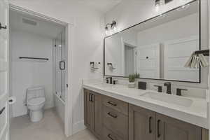 Bathroom featuring double vanity, shower / bath combination with glass door, and light tile patterned flooring