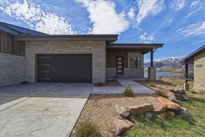 View of front of house with a mountain view, concrete driveway, an attached garage, stone siding, and covered porch
