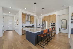 Kitchen featuring light wood-type flooring, a kitchen breakfast bar, a kitchen island with sink, dual tone cabinets, and stainless steel appliances