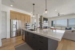 Dual tone kitchen with open floor plan, stainless steel appliances, a stone fireplace, hanging light fixtures, and a center island with sink