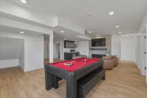Rec room featuring billiards table, light wood finished floors, a stone fireplace, and recessed lighting