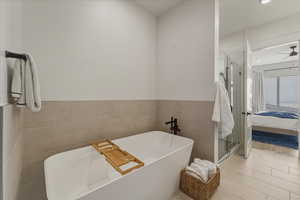 Full bathroom featuring ensuite bath, tile walls, a shower stall, a soaking tub, and a ceiling fan