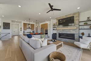 Living area with light wood-style flooring, a stone fireplace, a ceiling fan, and recessed lighting