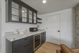 Bar area with beverage cooler, glass fronted cabinets, light wood-style floors, and open shelves