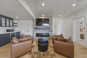 Living area featuring light wood-style flooring, a stone fireplace, recessed lighting, beverage cooler, and wet bar