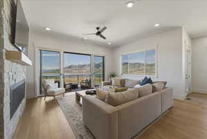 Living area featuring a stone fireplace, light wood-type flooring, a ceiling fan, and recessed lighting