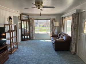 Sitting room featuring a ceiling fan, dark carpet, healthy amount of natural light, and a textured ceiling