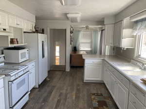 Kitchen featuring white appliances, white cabinets, light countertops, a peninsula, and dark wood-style flooring