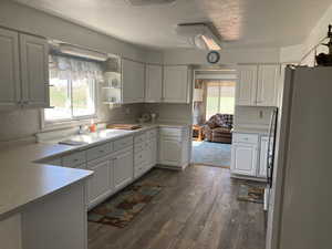 Kitchen with freestanding refrigerator, dark wood-type flooring, light countertops, white cabinets, and a textured ceiling