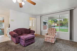 Living area with a ceiling fan, a textured ceiling, and carpet flooring
