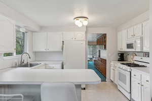 Kitchen featuring white appliances, light countertops, a peninsula, a breakfast bar area, and a textured ceiling