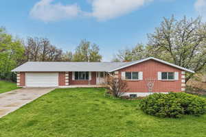 Single story home featuring driveway, a porch, brick siding, a garage, and a front yard
