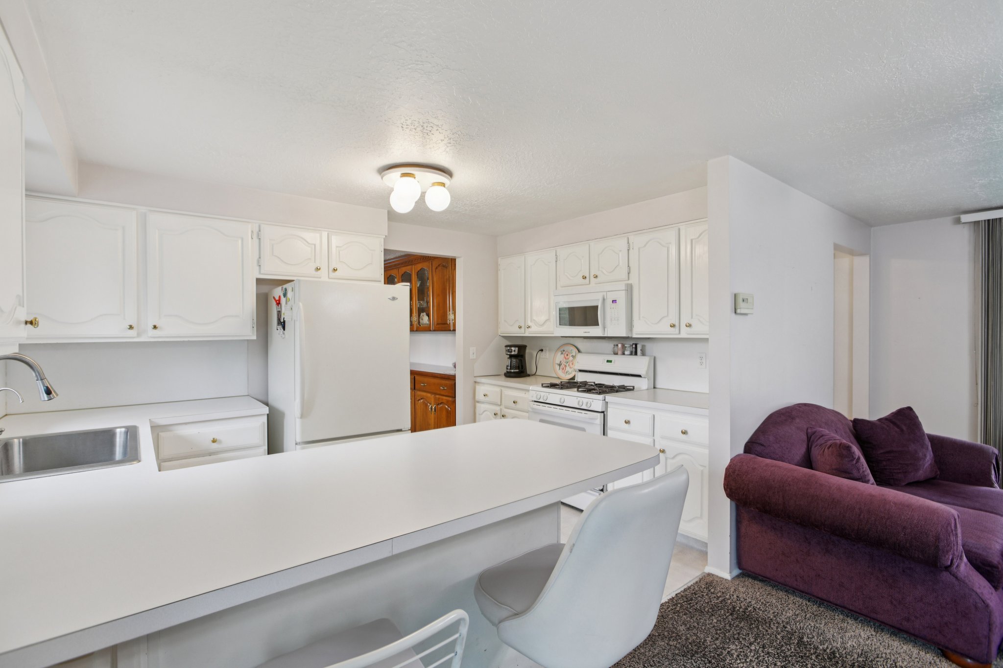 Kitchen with a kitchen breakfast bar, white cabinetry, white appliances, a peninsula, and a textured ceiling