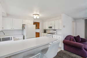 Kitchen with a kitchen breakfast bar, white cabinetry, white appliances, a peninsula, and a textured ceiling