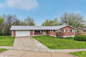 Single story home featuring driveway, brick siding, and a front yard