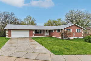 Ranch-style house with a front yard, concrete driveway, brick siding, and an attached garage