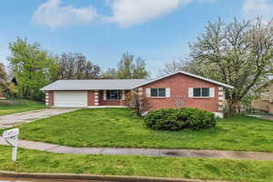 Ranch-style home with a front lawn, a garage, brick siding, and concrete driveway