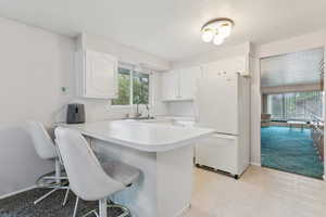 Kitchen with a kitchen bar, freestanding refrigerator, white cabinetry, light countertops, and a peninsula