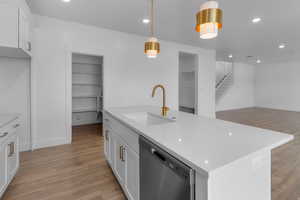 Kitchen with white cabinets, stainless steel dishwasher, a kitchen island with sink, light wood finished floors, and light stone countertops